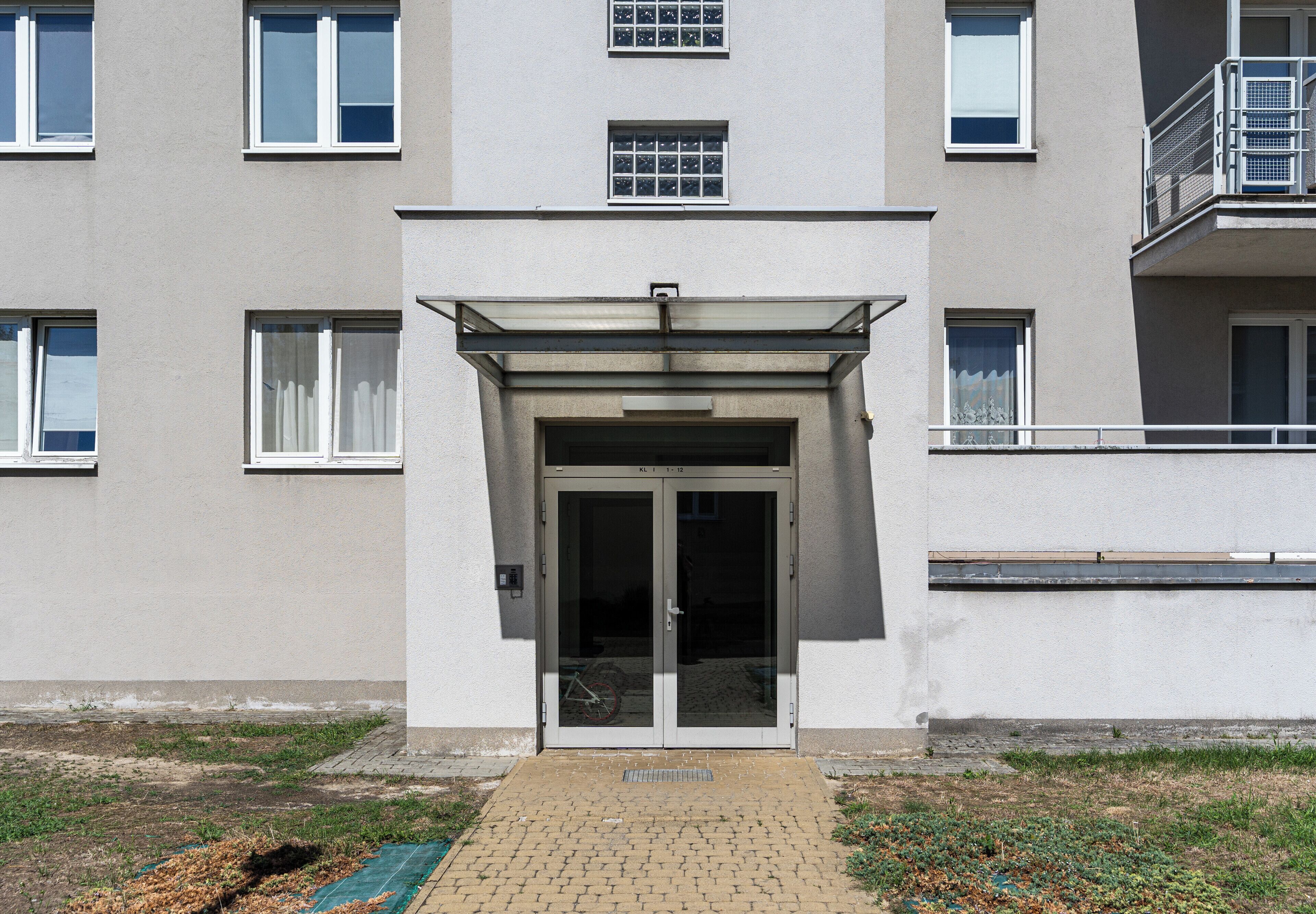 A building with a central entrance, multiple windows, and a paved area in front.