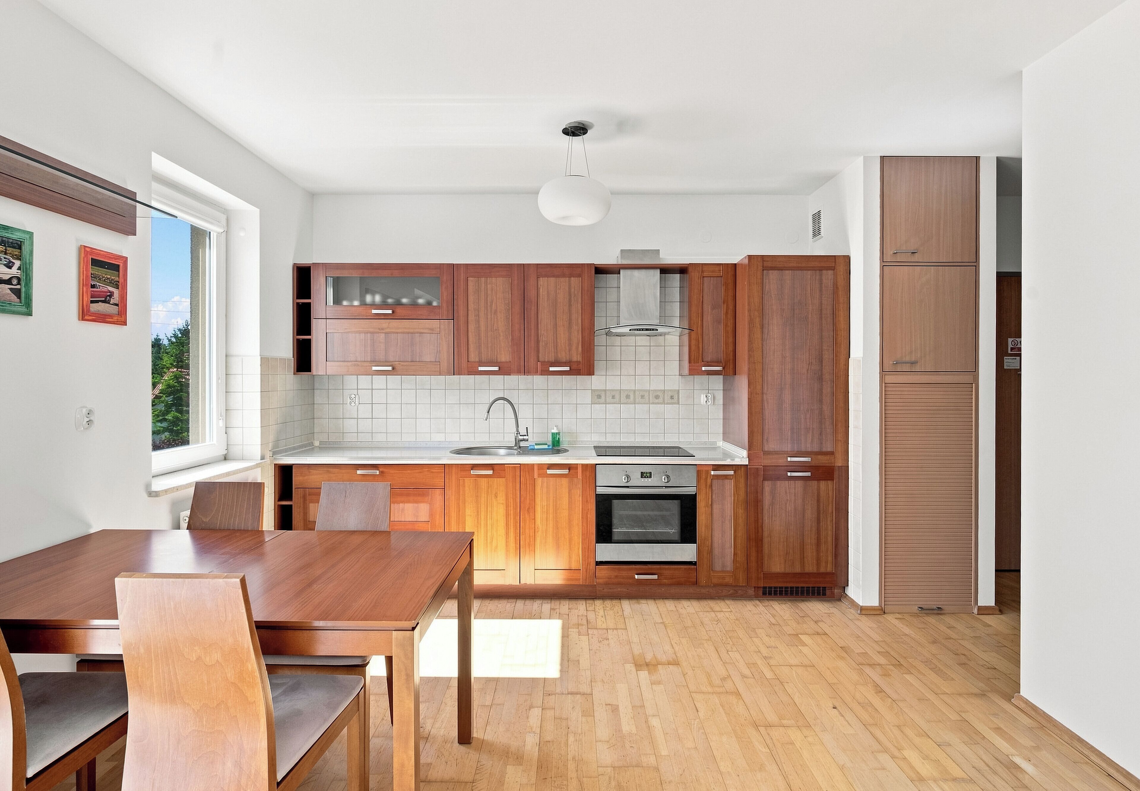 Eine moderne Küche mit Holzschränken, einem Einbauofen und einem Essbereich mit Holztisch und Stühlen.