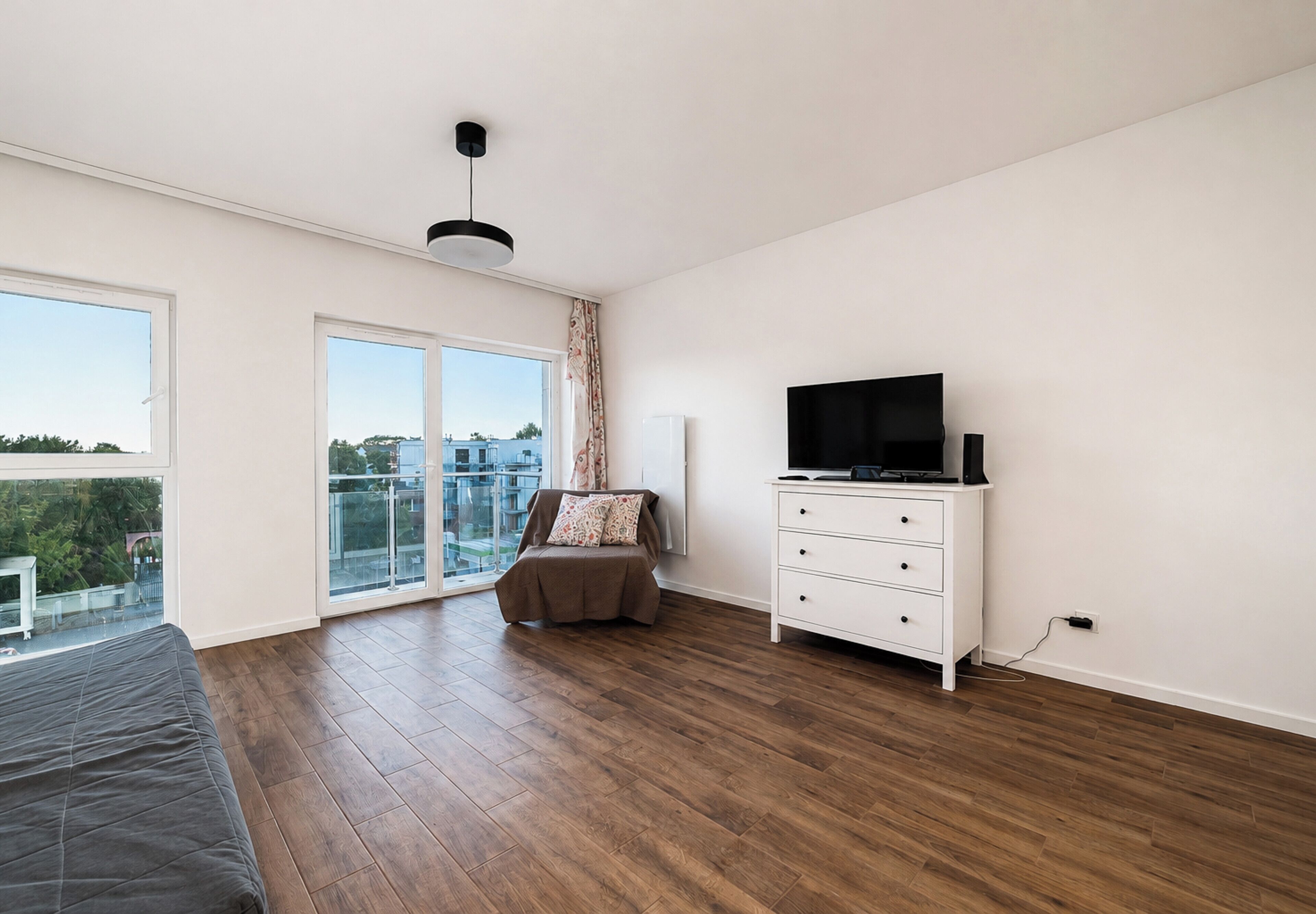 Un dormitorio moderno con un ventanal grande, un televisor de pantalla plana sobre un tocador blanco y un balcón con vistas.