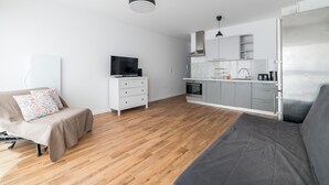 Um espaço de estar moderno e minimalista, com sofá, televisão, área de cozinha e mesa de jantar.
