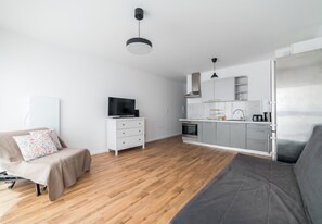 Ein moderner, minimalistischer Wohnraum mit Sofa, Fernseher, Küchenzeile und Esstisch.