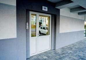 Une entrée d’immeuble avec une porte numérotée, une fenêtre en verre et un trottoir dallé.