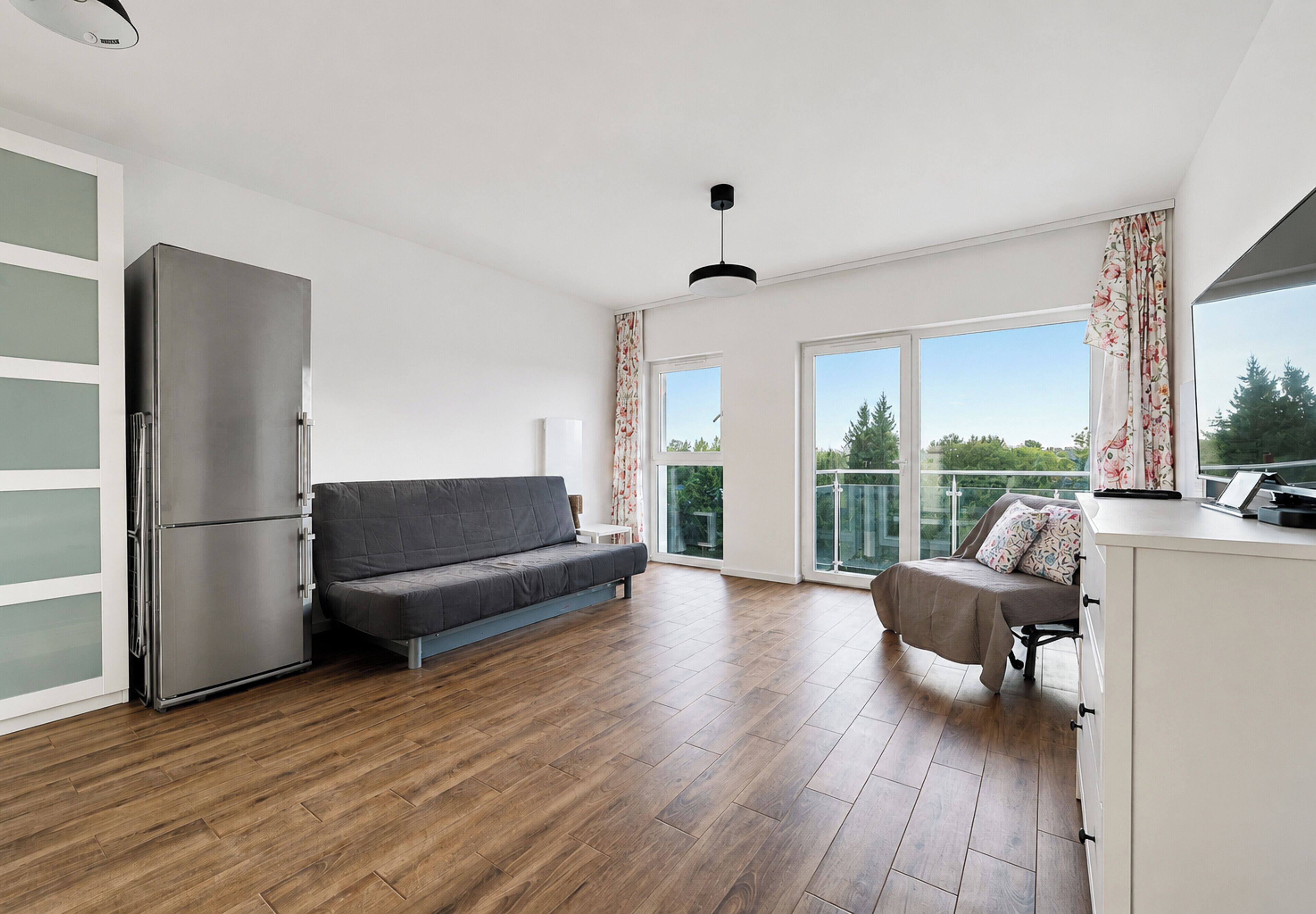 A modern kitchen with a built-in refrigerator, a grey sofa, and a dining area with a table and chairs. - Luboń City Comfort Studio (Luboń)