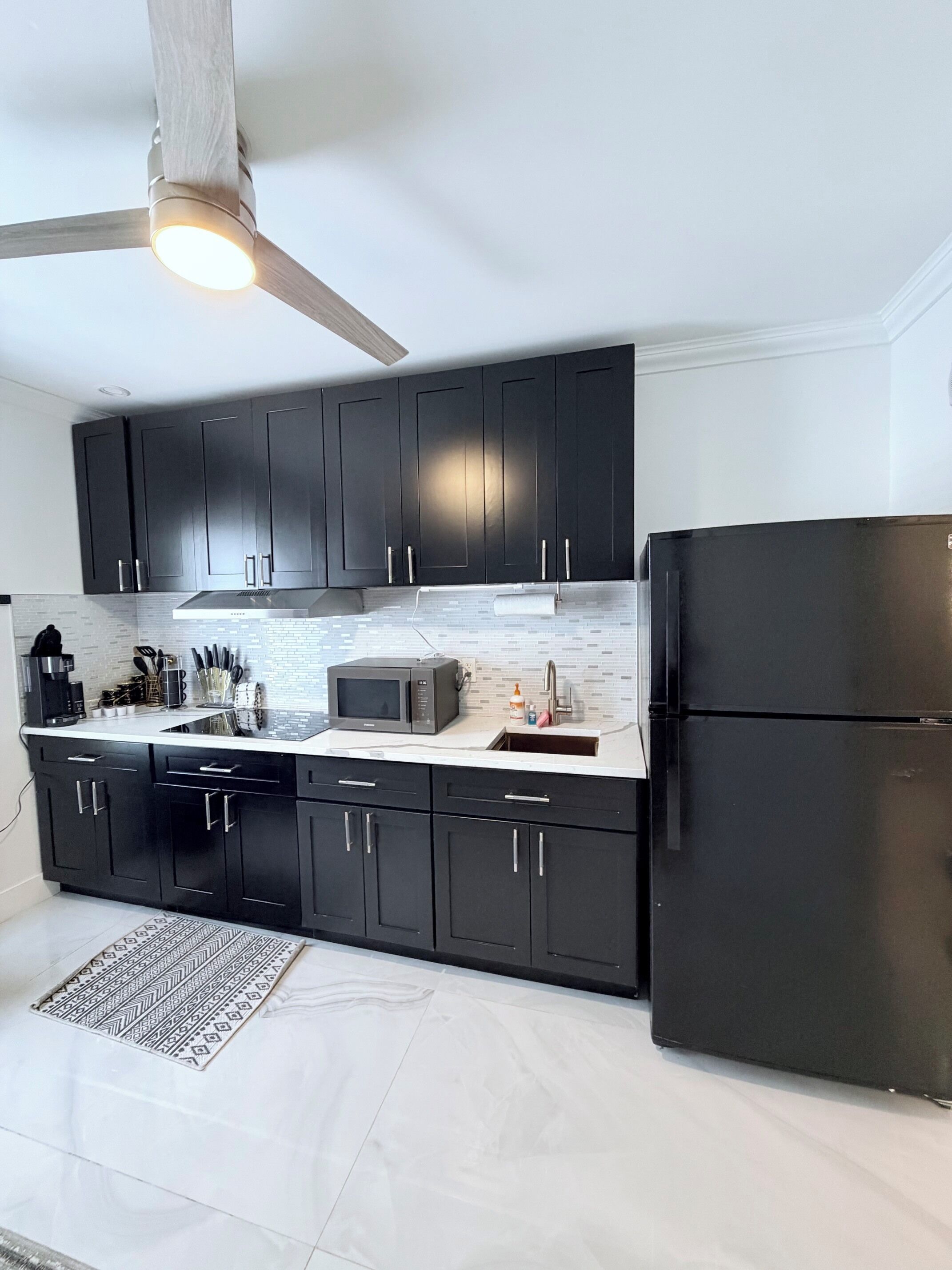 A modern kitchen with black cabinets, a stainless steel refrigerator, and a microwave.