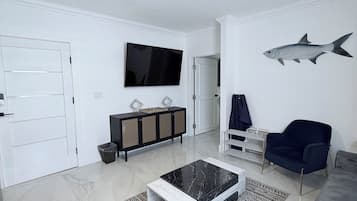 Una sala de estar moderna con ventilador de techo, televisor de pantalla plana, un cuadro de peces, un sofá oscuro, una mesa de centro y una alfombra estampada.