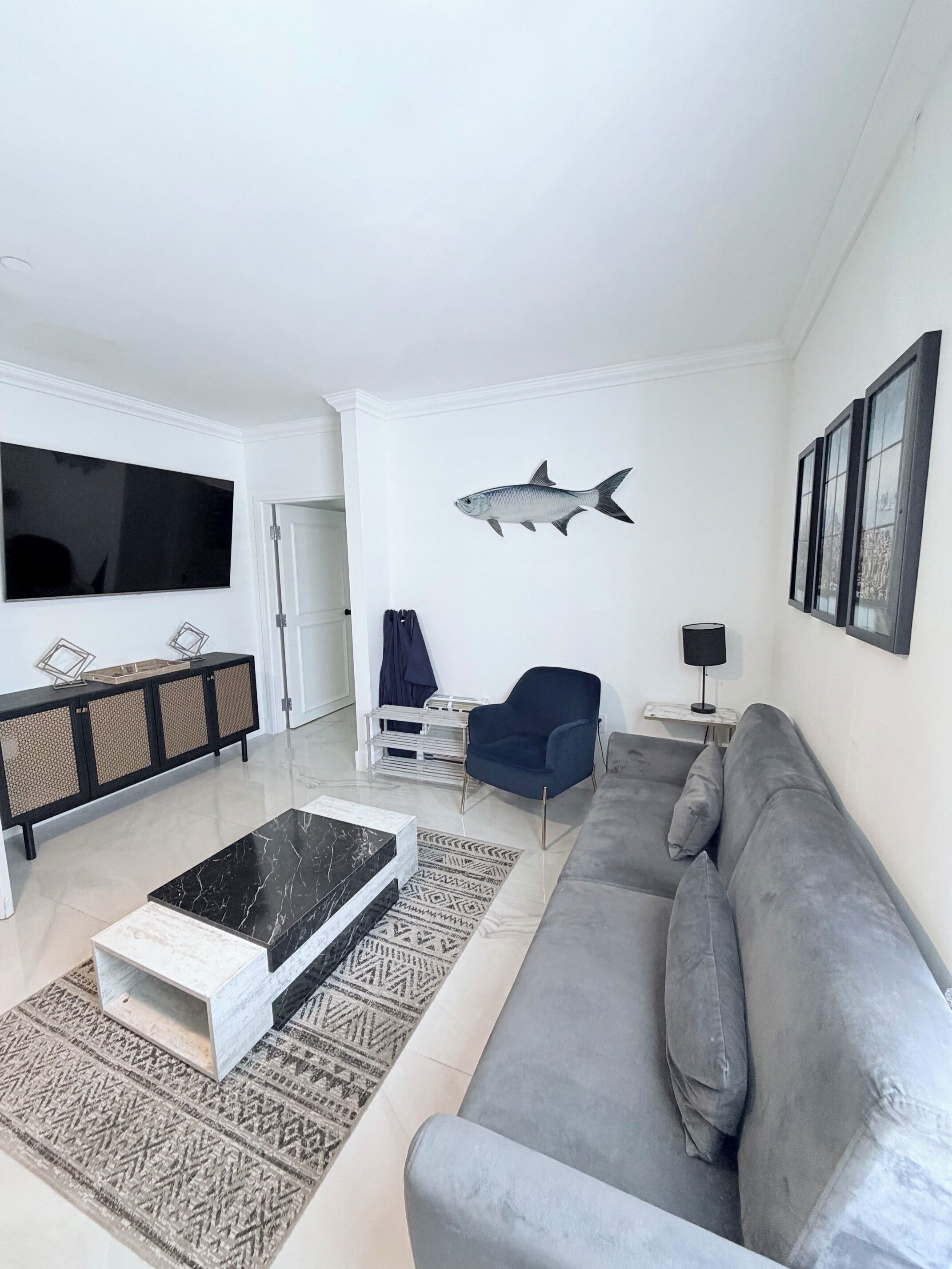 A modern living room with a flat-screen TV, a sofa, a coffee table, and a decorative fish wall art piece.