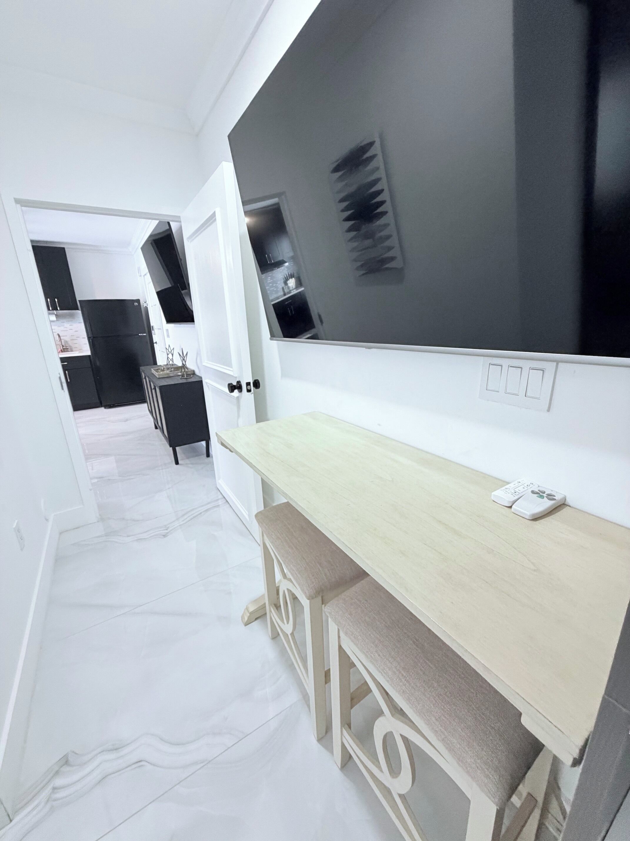A modern kitchen with a black refrigerator, white cabinets, and a wooden dining table with a bench.