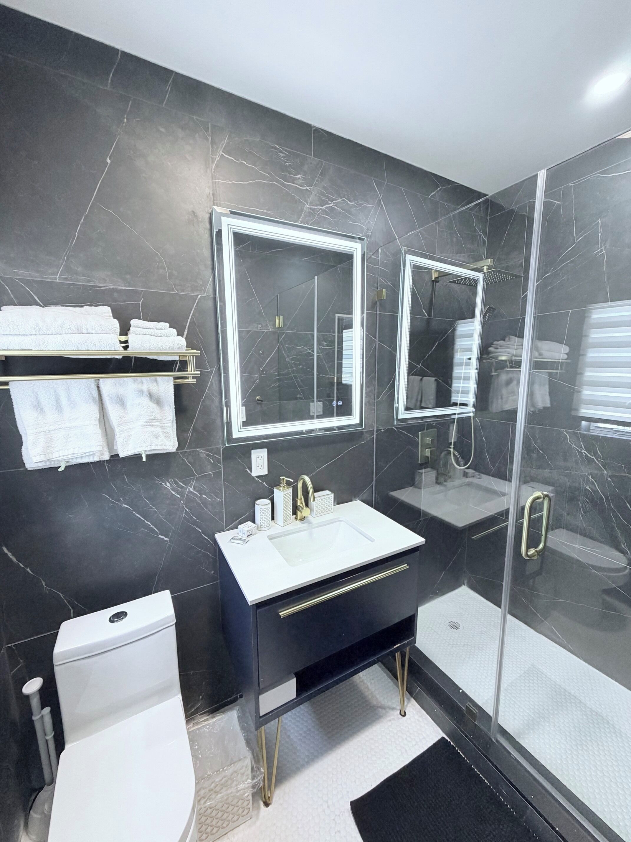 A modern bathroom with a black marble wall, a white sink, a glass shower enclosure, and a toilet.