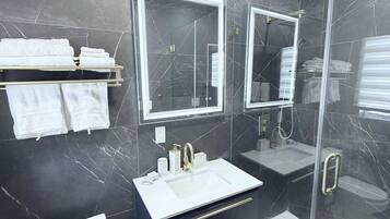 A modern bathroom with a black marble wall, a white sink, a glass shower enclosure, and a toilet.