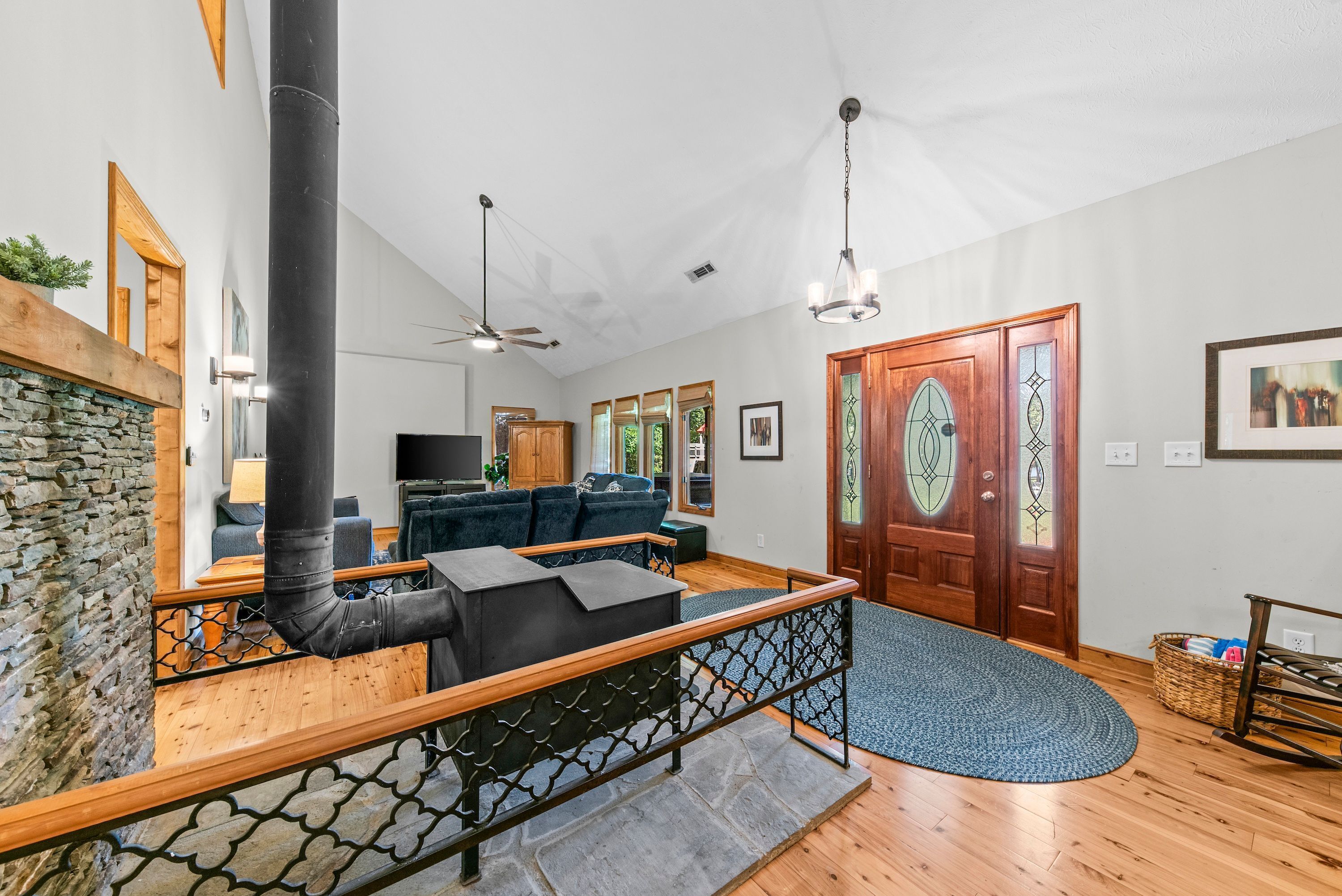 A spacious living area with a stone wall, a black pipe, a wooden bench, a blue rug, and a wooden door with glass panels.