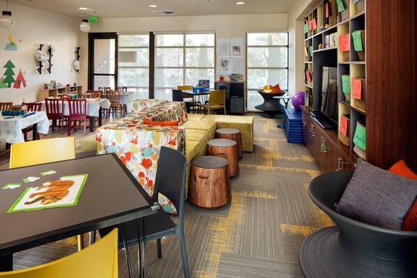 A well-lit indoor space with tables, chairs, a sofa, and a bookshelf.