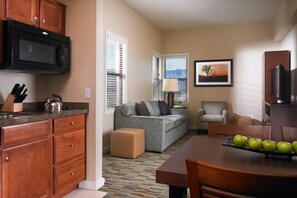 A compact living space with a kitchenette, a sofa, a dining table with apples, and a television.