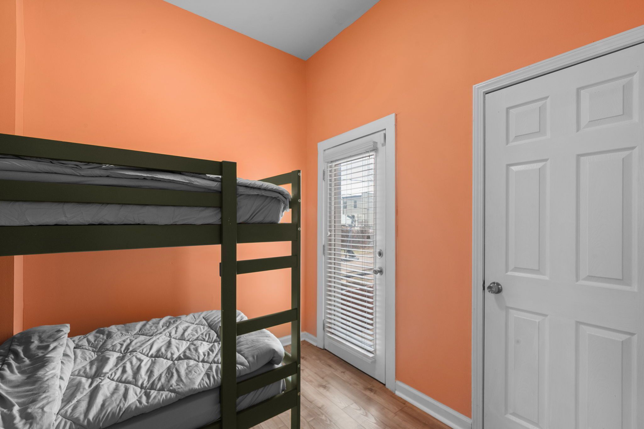 A room with a bunk bed, a door, and a window with blinds.