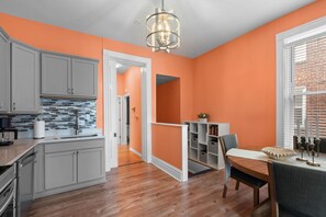 A kitchen with grey cabinets, a tiled backsplash, and a wooden floor. - Fun Grove Stay – Walk to Bars, Restaurants & BJC (St. Louis)