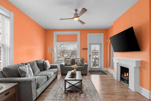 A living room with a grey sofa, a coffee table, a fireplace, and a TV mounted on the wall. - Fun Grove Stay – Walk to Bars, Restaurants & BJC (St. Louis)