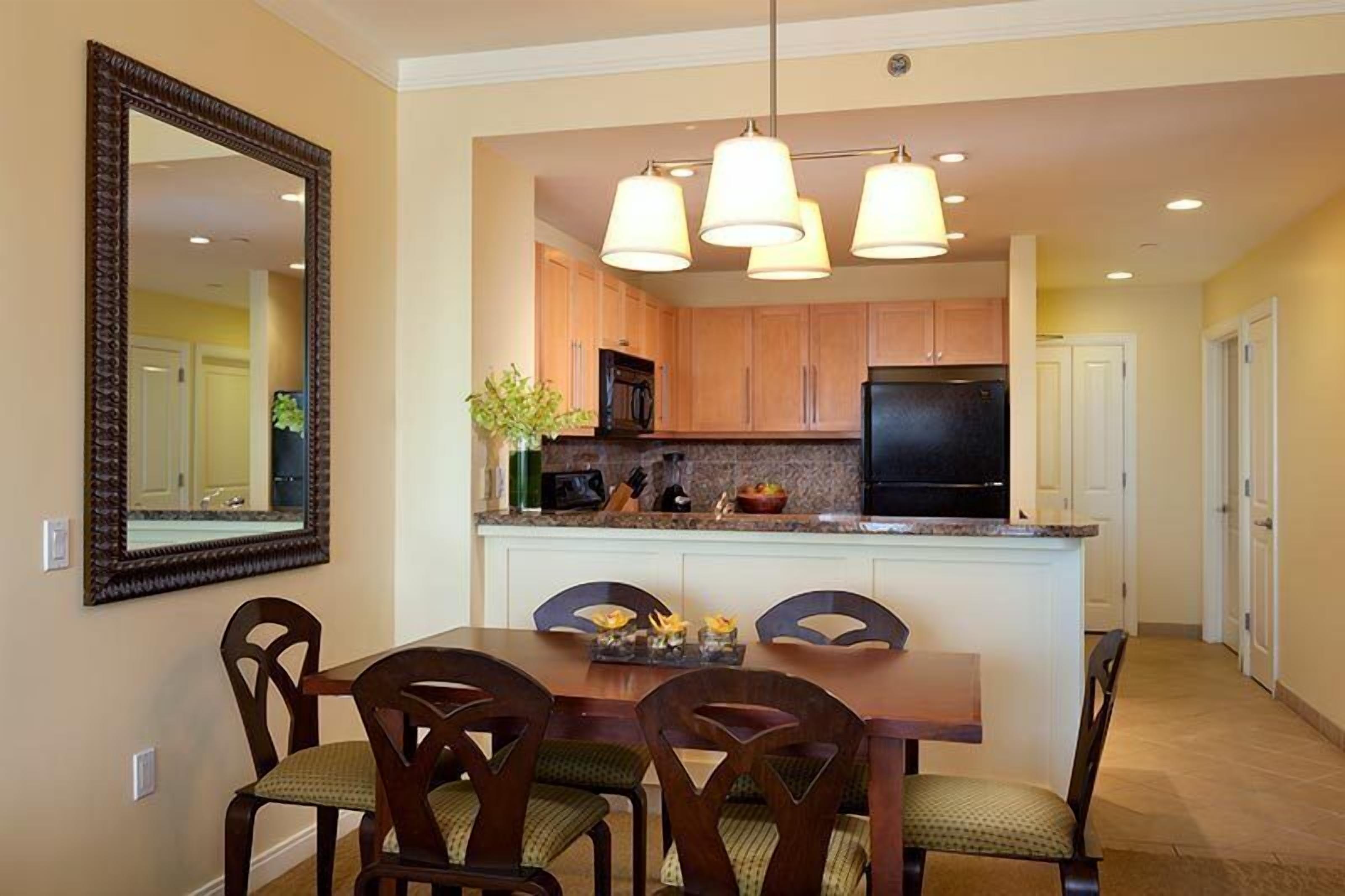 A dining area with a table and chairs, a kitchen with cabinets and appliances, and a large mirror on the wall.