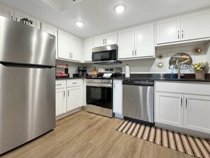 A modern kitchen with stainless steel appliances, white cabinetry, and a wooden floor. - Creekside walk to downtown, landing, king bed (Branson)
