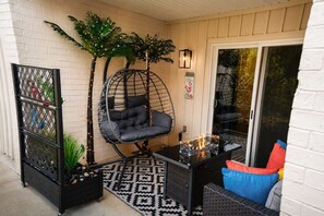 A cozy outdoor seating area with a hanging chair, a small table with a fire feature, and a decorative wall. - Creekside walk to downtown, landing, king bed (Branson)