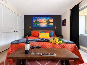Ein Hotelzimmer mit einem Bett, einem Gemälde an der Wand, einer Weinflasche, zwei Weingläsern und einer Schokoladentafel.