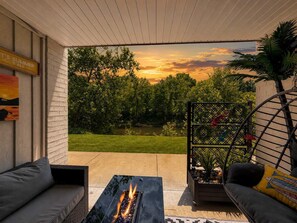 Eine Terrassenanlage mit Feuerstelle, Sitzgelegenheiten im Freien und Blick auf einen See bei Sonnenuntergang.