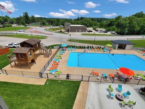 Ein Poolbereich mit rechteckigem Pool, Liegestühlen und einer hölzernen Spielanlage.