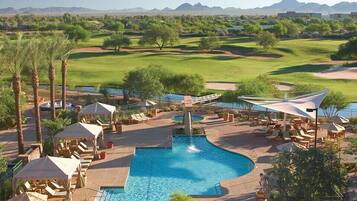 A pool area with lounge chairs and umbrellas, surrounded by a golf course and desert landscape.