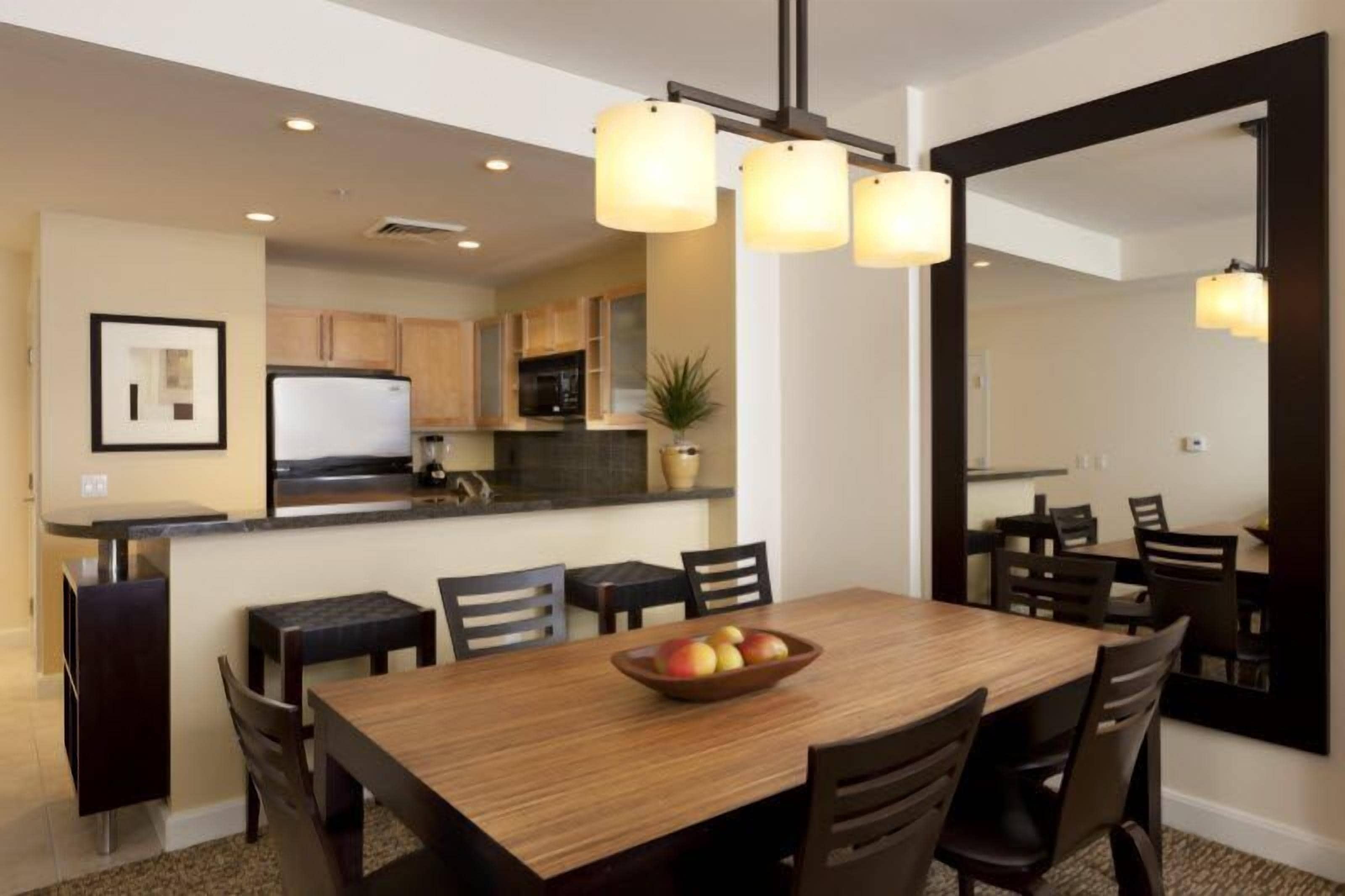 A dining area with a wooden table and chairs, a fruit bowl, and pendant lighting.