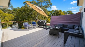 Eine Terrass mit überdachter Sitzecke, einem Tisch und einem großen Sonnenschirm.
