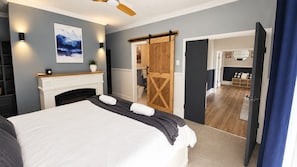 Ein Schlafzimmer mit Bett, Kamin, einer Schiebetür im Bauernhausstil und Blick in einen weiteren Raum.