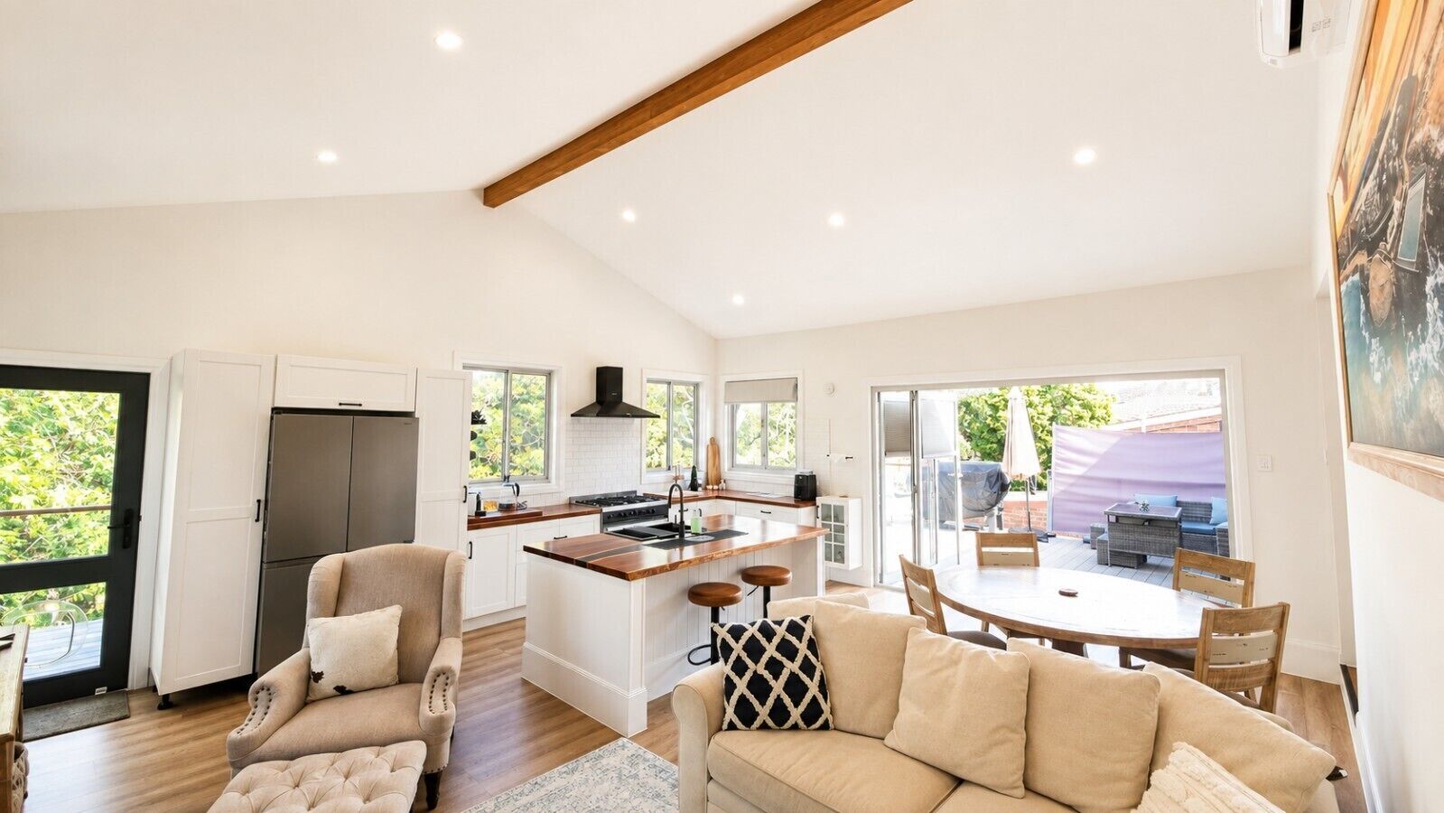 A modern kitchen with a central island, a dining area with a round table, and a living room with a sofa and armchairs.