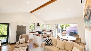 A modern kitchen with a central island, a dining area with a round table, and a living room with a sofa and armchairs.