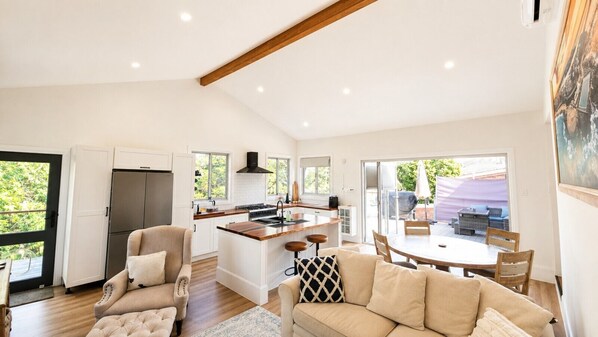 A modern kitchen with a central island, a dining area with a round table, and a living room with a sofa and armchairs.