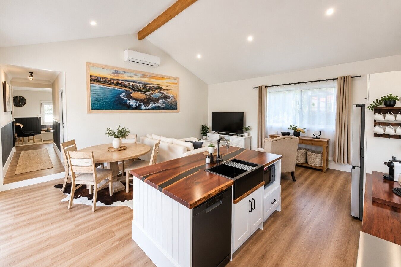 A modern kitchen with a central island, dining area with a round table, and a living space with a sofa and TV.