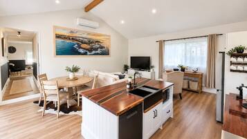A modern kitchen with a central island, dining area with a round table, and a living space with a sofa and TV.