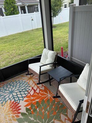 A patio area with a wicker sofa and a small table, a colorful rug, and a view of a white fence and grass. - Fantastic 2-bedroom townhome  Jacksonville (Jacksonville)