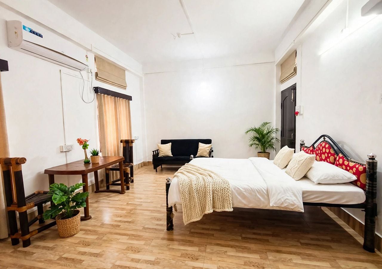 A bedroom with a bed, a wooden table, a bench, and a potted plant.