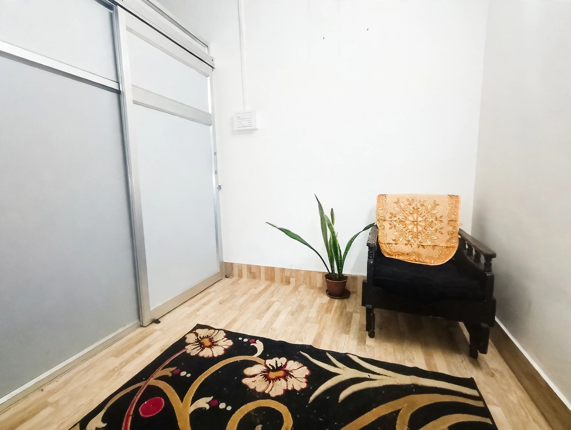 Une pièce avec un plancher en bois, une chaise noire avec un coussin à motifs, une plante en pot et un tapis décoratif.