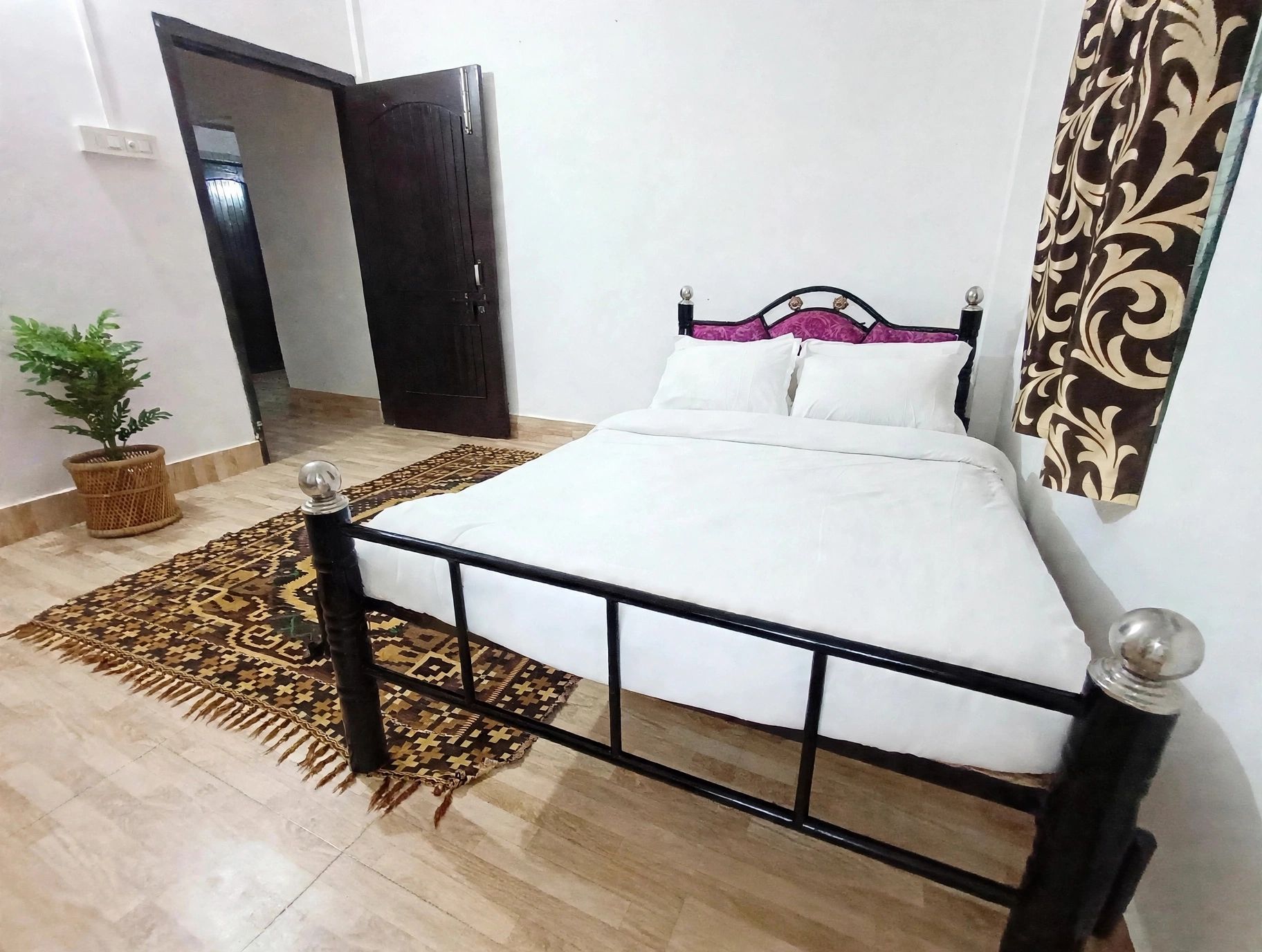 Un dormitorio con una cama, un tapete estampado, una planta en maceta y una puerta.
