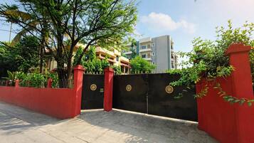 Una entrada protegida con un muro rojo y un portón negro, que conduce a un edificio con varios pisos y balcones.