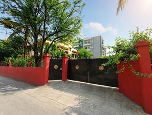 Una entrada protegida con un muro rojo y un portón negro, que conduce a un edificio con varios pisos y balcones.