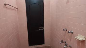 Une salle de bain avec des murs recouverts de carreaux roses, une porte noire et un espace douche équipé d’un pommeau de douche à main.