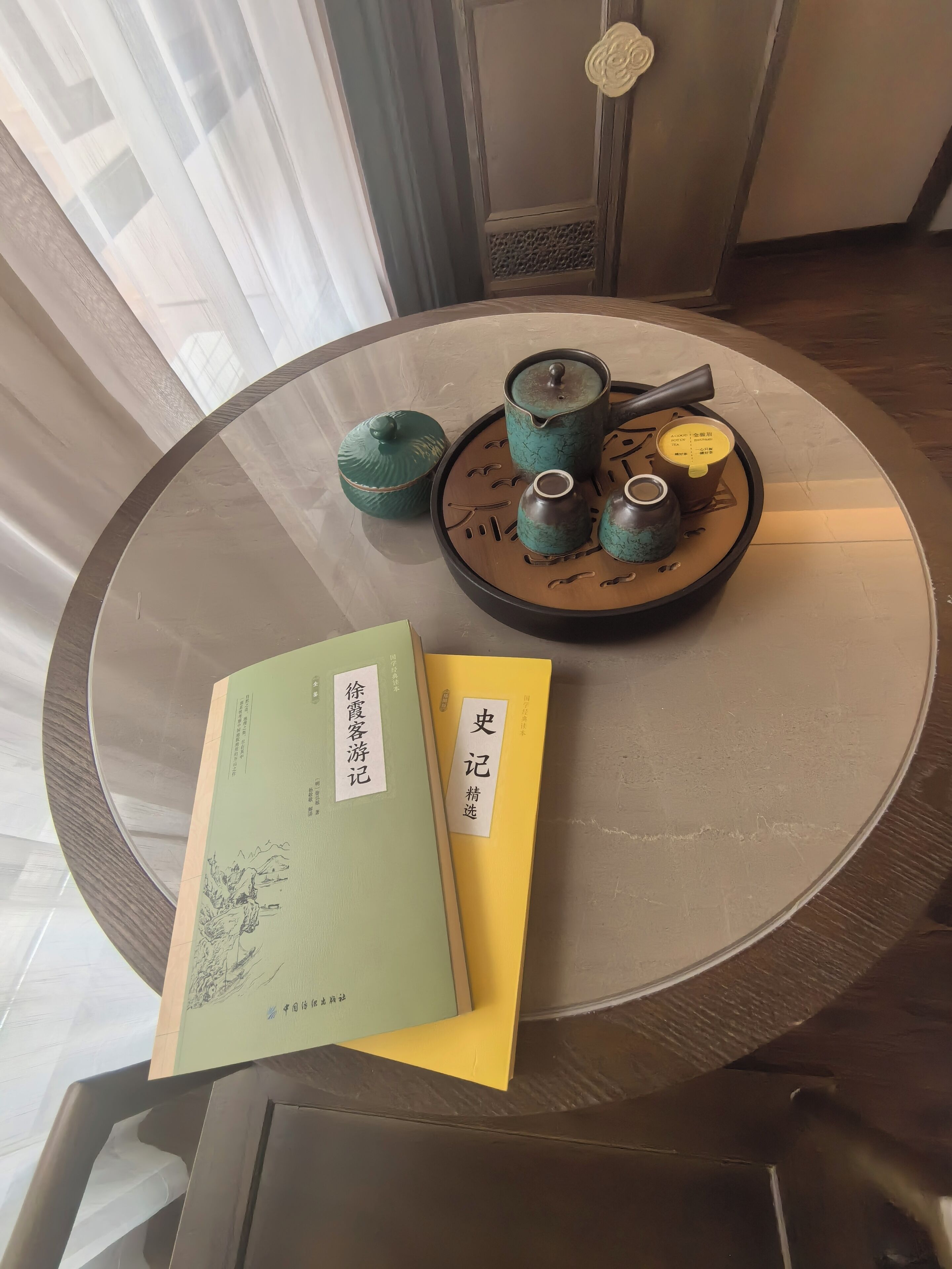 Une table ronde avec un service à thé, deux livres et un objet décoratif.