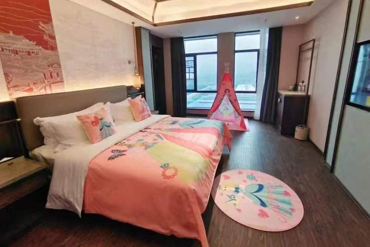 A hotel room with a large bed, a small table, and a window with a view.