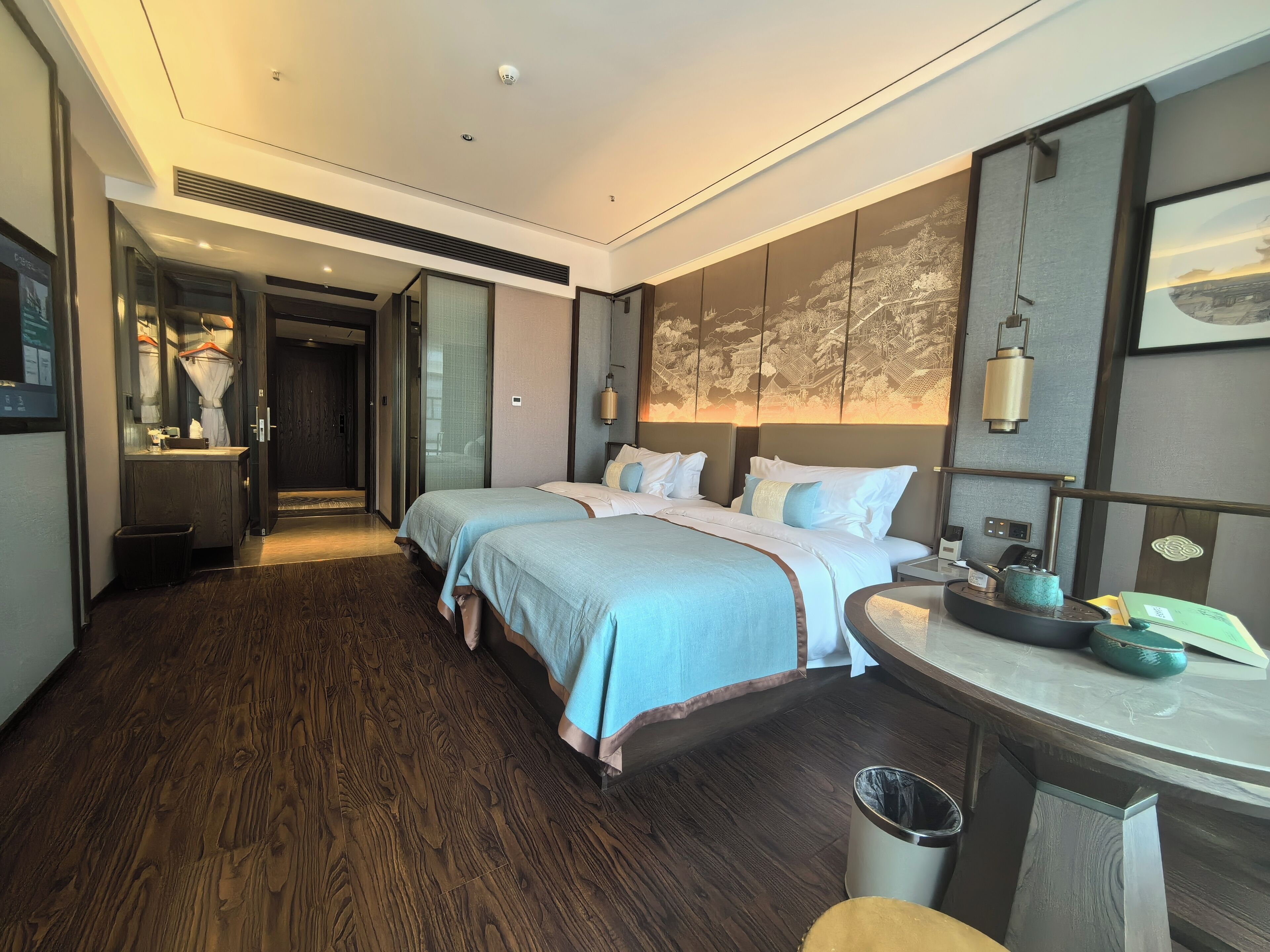 Habitación de hotel con dos camas, un escritorio, un cesto de basura y una lámpara de pared.