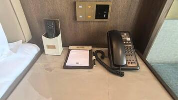 Habitación de hotel con mesita de noche, teléfono, control remoto y un cartel con código QR.