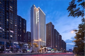 A high-rise building with illuminated signage, surrounded by other tall buildings and a busy street with moving vehicles.