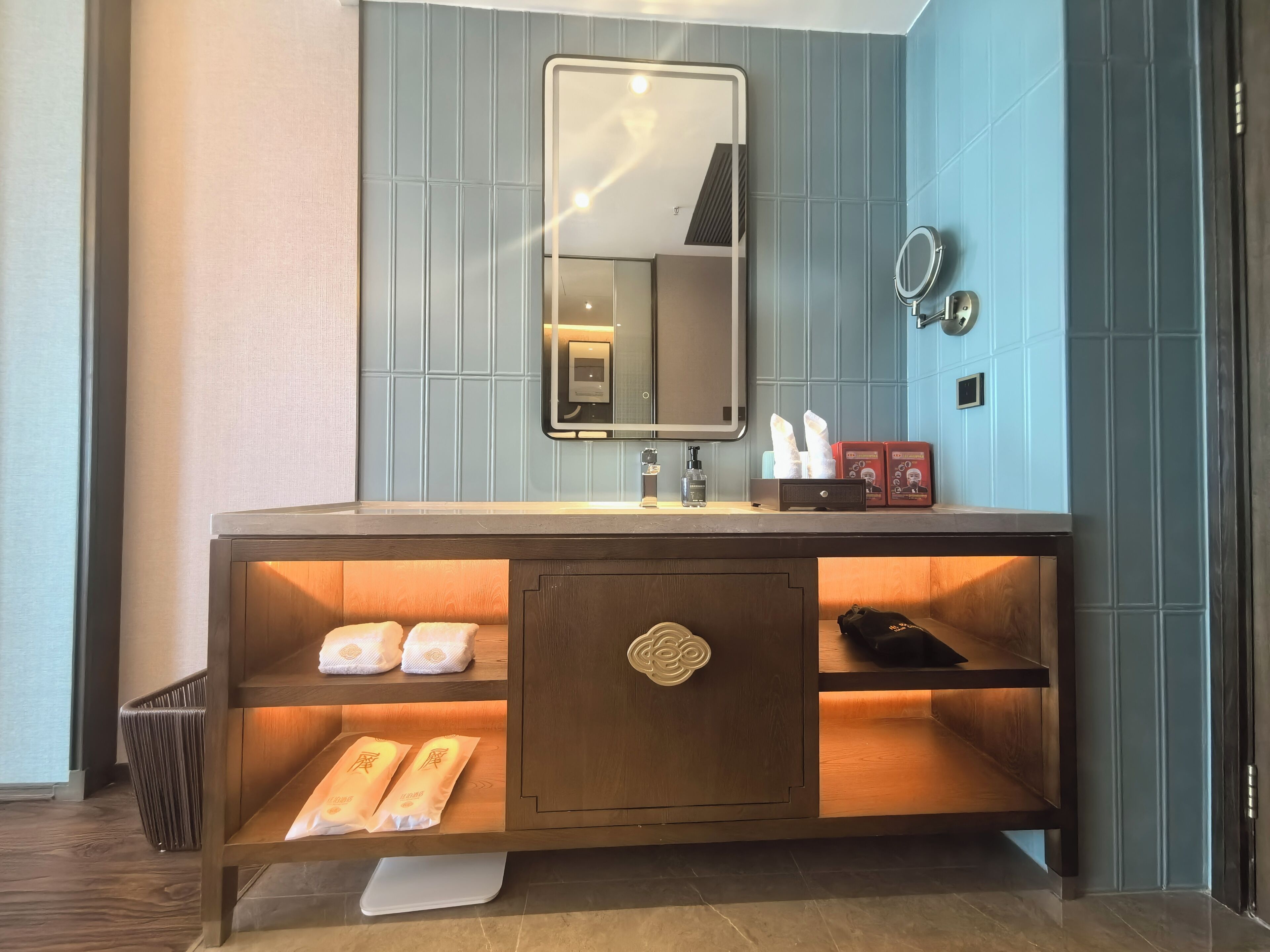 A modern bathroom with a wooden vanity, a mirror, a towel rack, and a shelf with toiletries.
