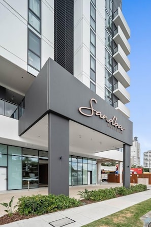 A hotel entrance with a modern facade, large windows, and a clear sky. - City Views, Ocean Hues | Sandbar (Gold Coast)