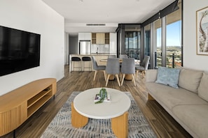 A modern living room with a flat-screen TV, a round coffee table, and a sofa. - City Views, Ocean Hues | Sandbar (Gold Coast)