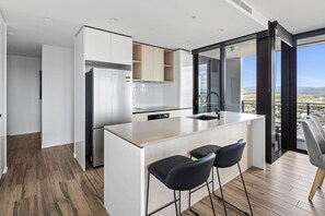 A modern kitchen with a central island, bar stools, and a view of the city. - City Views, Ocean Hues | Sandbar (Gold Coast)